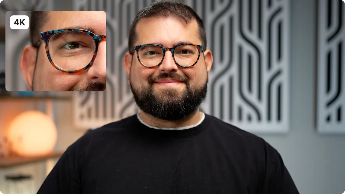 Smiling man with a beard wearing tortoiseshell glasses and a black shirt in front of a patterned gray wall.